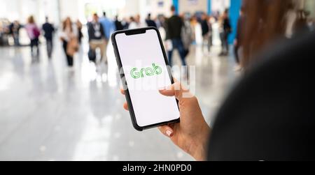 Woman hand holding iphone Xs with logo of Grab application in a pedestrian zone. Grab is smartphone app all-in-one transport booking in South-East Asi Stock Photo