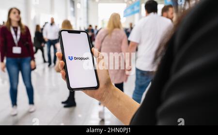 Woman hand holding iphone Xs with logo of Dropbox application. Dropbox is a file hosting service operated by Dropbox Stock Photo
