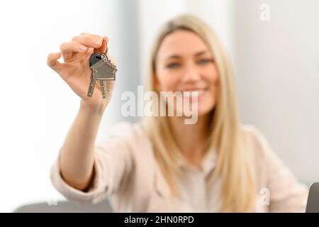 Selective focus on the keys with keychain in form of small cute house in hand of caucasian female. Blonde woman bought own property, relocating in modern bright flat Stock Photo