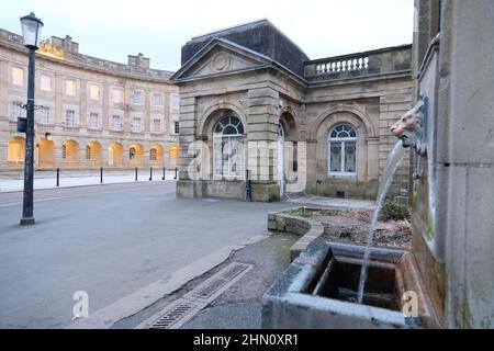 Drinkable Buxton spring water emanating from lion's head fountain at St Ann's Well with Buxton Crescent hotel and Pump Room in the background Stock Photo