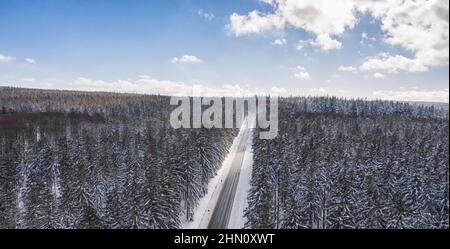 Aerial view of cars driving by the road through the forest covered by snow in winter and cloudy sky, including Copy space Stock Photo