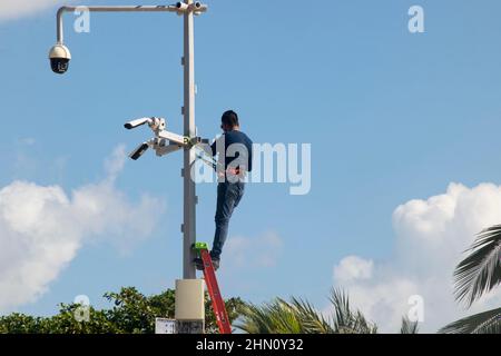 A Specialist on a metal ladder installs security cameras near a public beach in Mexico Stock Photo