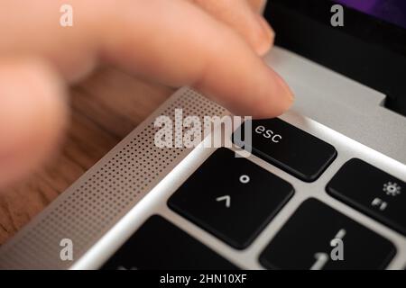 Hand pressing escape key on modern laptop keyboard. Esc sign and symbol closeup Stock Photo
