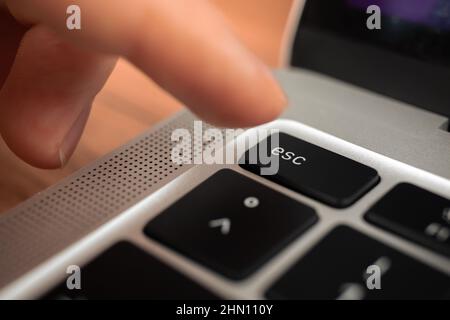 Hand pressing escape key on modern laptop keyboard. Esc sign and symbol closeup Stock Photo