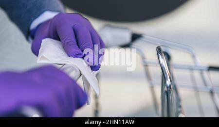 Hands with gloves using cloth with alcohol antiseptic, disinfecting spray, cleaning on shopping cart, trolley handle, protection during Coronavirus pa Stock Photo