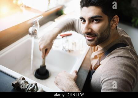 Handyman at work. Repairing kitchen sink by plunger. man trying to fix kitchen sink. Stock Photo