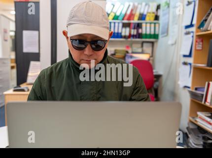 A man using a laptop online wearing sunglasses and a cap. Cyber crime, security, financial scams concept. Stock Photo