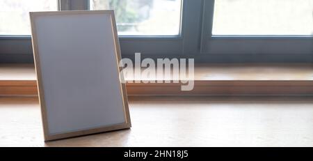 Picture frame empty on a wooden table, home interior decoration, glass window background, copy space. Stock Photo