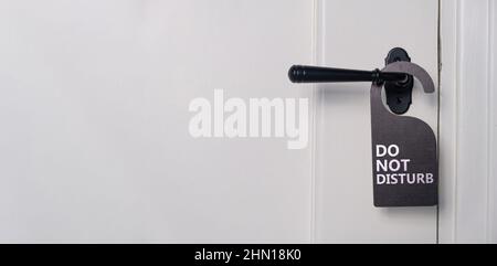 Do not disturb text sign, hotel room hanger. Black label on closed retro paneled door handle, close up view. White wooden doorway Stock Photo