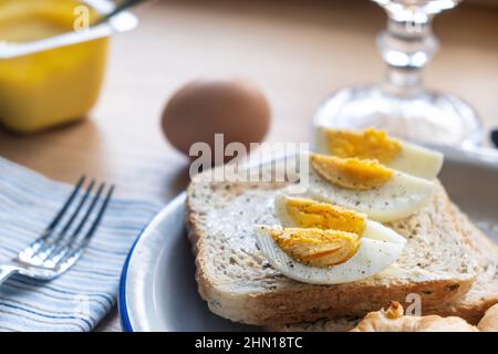Boiled eggs on toast bread with butter and yogurt. Healthy breakfast proteins and nutrition on a wooden table, close up view Stock Photo