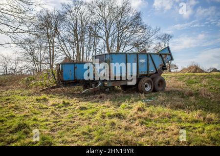 A pair of blue old and rusty trailers parked in an agricultural field in rural Norfolk Stock Photo