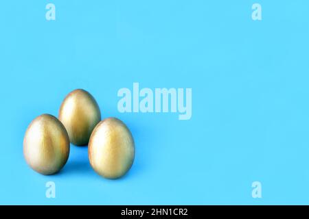 Easter eggs on blue background. Three golden eggs. Minimal style. Easter decorations. Stock Photo