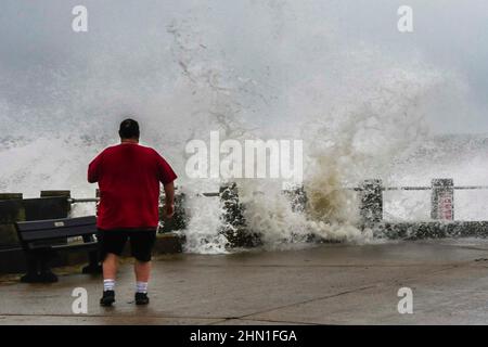 West Bay Dorset, UK.  13th February 2022.  UK Weather.  A man watches as the stormy seas crash against the sea defences at West Bay in Dorset on an afternoon of heavy rain and gale force winds.  Picture Credit: Graham Hunt/Alamy Live News Stock Photo