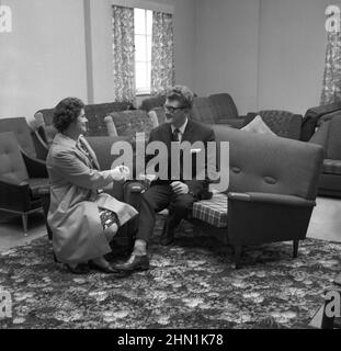 1960s, historical, inside a furniture shop, a lady shaking the hands of a suited salesman for his help after buying a new settee and lounge chairs, known as a 'three piece suite'. Stock Photo