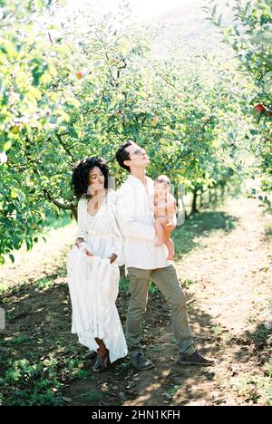 Woman stands next to a man with a baby in his arms in the garden Stock Photo