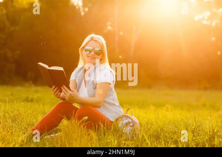 against background of green meadow grass sat young, charming girl, student reads book Stock Photo