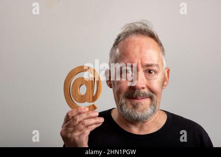 middle-aged man with in hand real email symbol carved in wood, in gray background Stock Photo