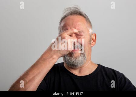 the middle-aged man holds his hand firmly on his nose to plug the horrible smell he is smelling. Isolated on gray background with space for your copy Stock Photo