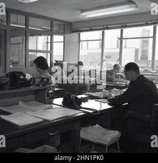 1950s, historical, inside view of administration staff at work in the offices of  a steel manufacturing company, Abbey Works, Port Talbot, Wales, UK. Men and women employees at their desks, with paperwork. A cigarette burning in ashtray beside a male worker and a bakerlite telephone of the era. Stock Photo