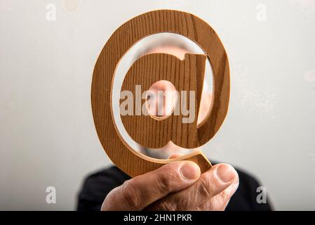 middle-aged man with in hand real email symbol carved in wood, in gray background Stock Photo