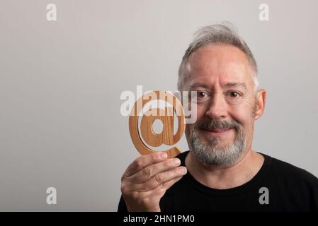 middle-aged man with in hand real email symbol carved in wood, in gray background Stock Photo