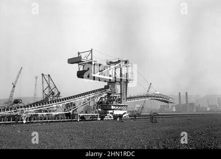 A view of massive machines used to move coal and coke at the Port Talbot Steelworks, an integrated steel production plant in Port Talbot, West Glamorgan, Wales, UK c. 1970. The constant need for massive amounts of fuel for the furnaces meant huge pieces of conveyor-belt equipment were required at the works – a vintage 1960s/70s photograph. Stock Photo