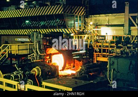 A mid-1980s view inside the Port Talbot Steelworks, an integrated steel production plant in Port Talbot, West Glamorgan, Wales, UK. Inside the mill hot sheet-steel is being rolled out on the production line. The Mill Control Centre is in the background. This image is from a vintage colour transparency – a vintage 1980s photograph. Stock Photo