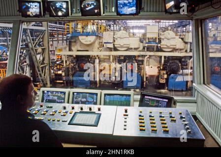 A mid-1980s view inside the Port Talbot Steelworks, an integrated steel production plant in Port Talbot, West Glamorgan, Wales, UK. This is a view from the Mill Control Centre looking out onto the milling machinery on the shopfloor. TV monitors relay information to the controller at his desk. This image is from a vintage colour transparency – a vintage 1980s photograph. Stock Photo