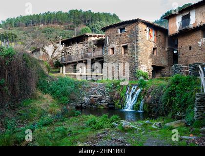 Typical rustic architecture of Robledillo de Gata, small waterfall, slate house and pine forest in the background horizontal Stock Photo