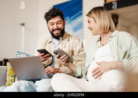 Bearded man and pregnant woman using cellphones while sitting on couch at home Stock Photo