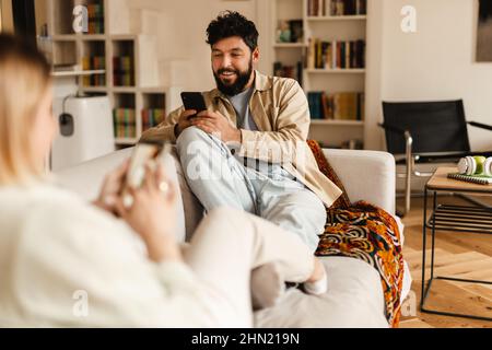 White couple using cellphones while sitting on couch at home Stock Photo