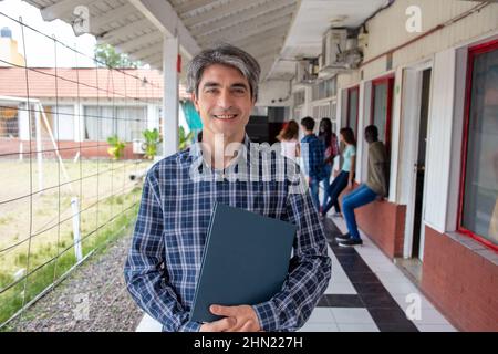 Hight school teacher looking to the camera in the hallway, students talking in the background Stock Photo