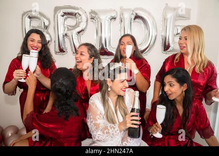 Bride and godmothers together with glass of champagne in hand in portrait against white background. Salvador, Bahia, Brazil. Stock Photo