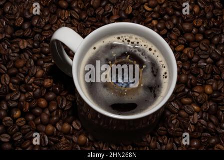 The picture shows a cup of coffee with a falling milk drop. In the background are coffee beans. Stock Photo