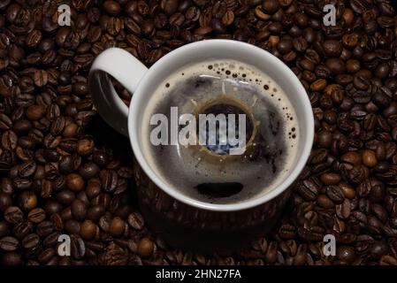 The picture shows a cup of coffee with a falling milk drop. In the background are coffee beans. Stock Photo