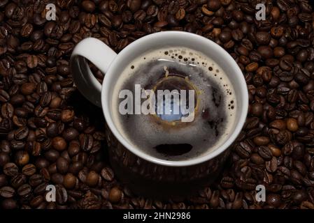 The picture shows a cup of coffee with a falling milk drop. In the background are coffee beans. Stock Photo