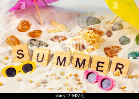Word Summer on yellow sandy textured background with bright seashells and stones. Sea holiday tourism and tropical vacations concept. Stock Photo