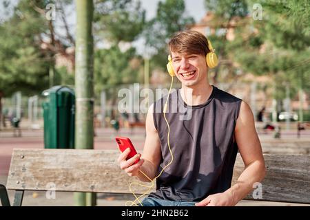 Cheerful young sportsman making video call on his smartphone with earphone - young fit male taking a selfie after exercising Stock Photo