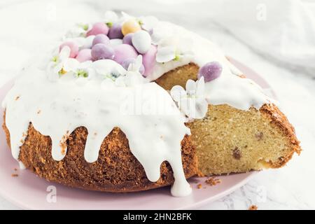 Glazed easter cake decorated with flowers and mini chocolate eggs candy on white marble background. Happy Easter Holidays. Stock Photo