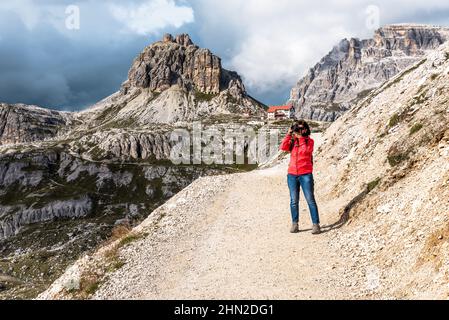 Woman hiker taking photos from a high altitude mountain path in the European Alps in autumn. Storm clouds are looming on horizon. Stock Photo