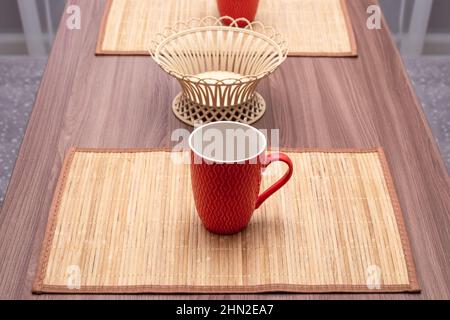 Wooden table with decorative napkins and red cups for tea. Dining room interior. Stock Photo