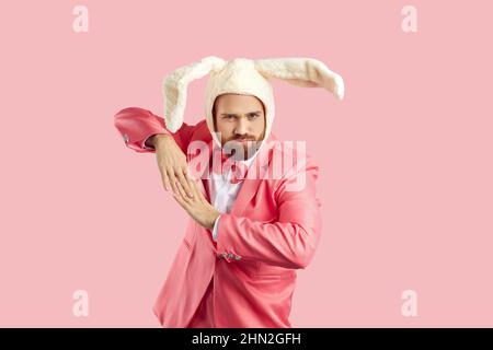 Cheerful man dressed in funny fluffy hat with rabbit ears having fun isolated on pink background. Stock Photo
