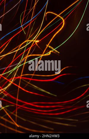 Drawing with light. Abstract multicolored rays on a black background. Curved wave lines. Vertical background. Stock Photo