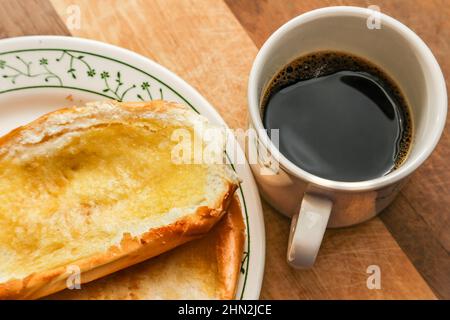 Goiânia, Goias, Brazil – February 13, 2022: Two buns on the plate and a cup of coffee on a wooden surface. Stock Photo