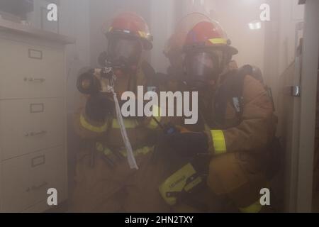 220203-N-VQ947-1067 PACIFIC OCEAN (Feb. 3, 2022) — Sailors battle a simulated fire in the ship’s library during a general quarters drill aboard San Antonio-class amphibious transport dock USS Portland (LPD 27), Feb. 3, 2022. Noble Fusion demonstrates that Navy and Marine Corps forward-deployed stand-in naval expeditionary forces can operate as a Marine Expeditionary Unit/Amphibious Ready Group team at sea, along with a carrier strike group, in order to conduct lethal sea-denial operations, seize key maritime terrain, guarantee freedom of movement, and create advantage for US, partner and allie Stock Photo