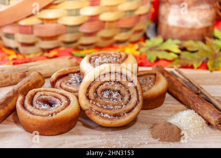 Festive fall setting of freshly baked pinwheel cinnamon rolls surrounded by cinnamon bark and fall colors. Stock Photo