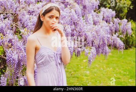 Girl with nose sneezing. Polen allergy symptom concept. Woman being allergic to blossom during spring front of blooming tree outside. Stock Photo