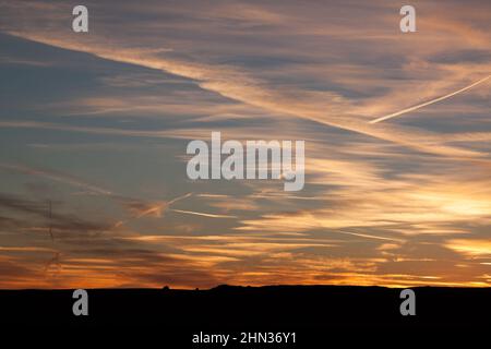 A brilliant sunset with contrails takes up the sky near Green River, Utah, with just a band of silhouetted black land at the bottom of the image Stock Photo