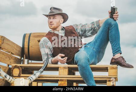 Cowboy wearing hat. Western life. Handsome bearded west farmer. Portrait of man cowboy or farmer. Western. Guy drinking whiskey. Stock Photo