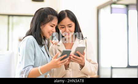 Two charming Asian businesswomen sharing their social media contact to each other in the office. Businesswomen using smartphone Stock Photo